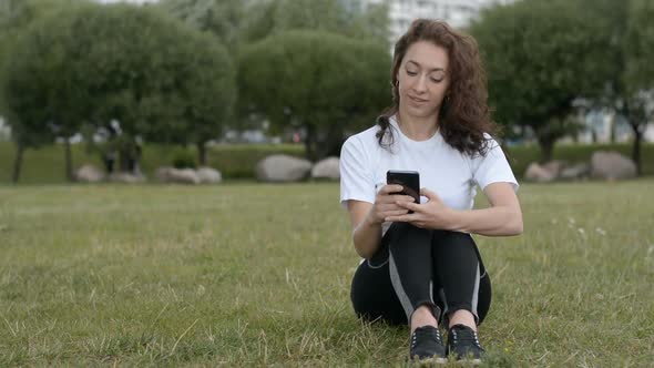 Girl in the Park Sits on the Grass and Writes a Message alt