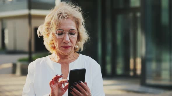 Smiling Blond Businesswoman Holding Digital Tablet in Front of Office Building alt