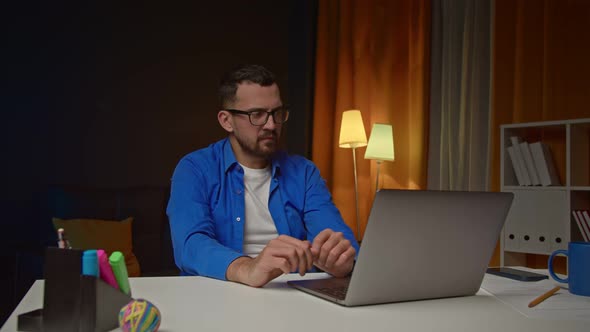 Tired Handsome Man Drinking Coffee and Looking on Computer Screen in Home Office alt