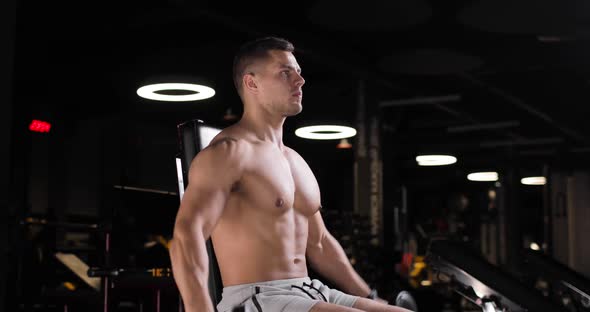 Athletic Young Man Exercising in the Gym Doing Strength Exercises with a Dumbbells in a Sitting