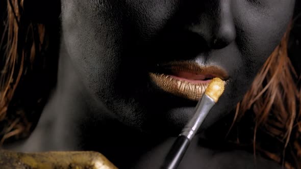 Closeup of a Woman with Black and Gold Paint and a Paintbrush Posing in Studio alt