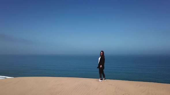 A Young Woman Walks Along Sandy Dunes on Seashore