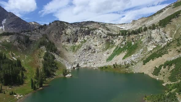Clouds move across a mountainside as the camera flies forward over a pond alt
