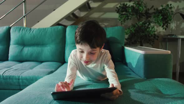 Adorable Kid Boy Using Digital Tablet Watching Cartoons Lying on Bed at Home. alt