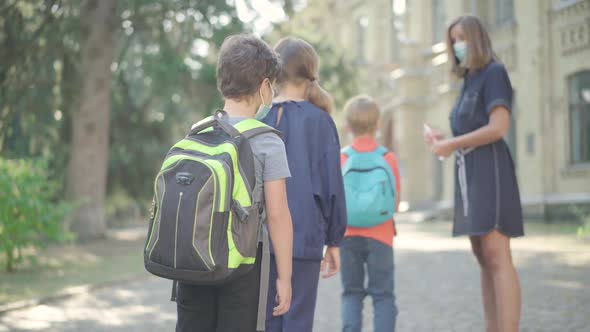 Teacher Spraying Sanitizer on Hands of Middle School Pupils Before Entering School. Caucasian Woman alt