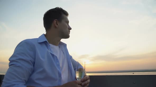 Pensive Young Man With Glass of Champagne Looking at Sunset From Terrace