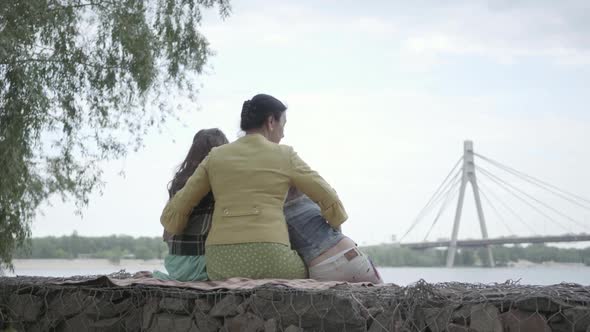 Portrait of Adorable Grandmother Who Sitting with Two Cute Granddaughters in the Bench alt