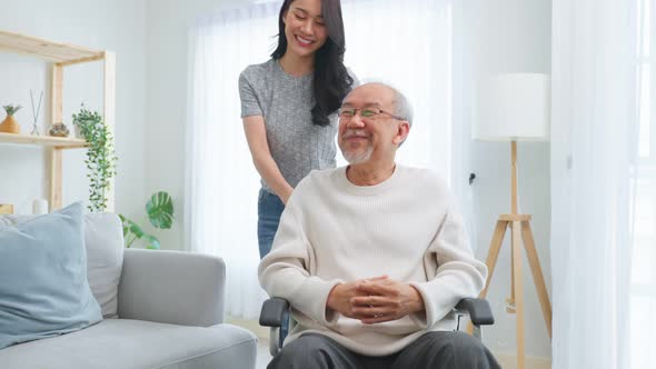 Asian young daughter take care senior male while sitting on wheelchair. alt