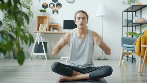 Portrait of Young Man Teaching Yoga Online Speaking and Demonstrating Exercise From Home alt