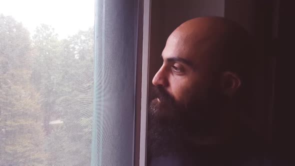 Young bearded caucasian man indoor looking outside window alt