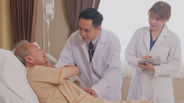 Asian doctor and nurse taking care of elderly male patient lying down on bed in recovery room. alt