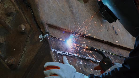 A man wearing a welding mask and gloves works in a home workshop with a welding machine. Worker weld alt