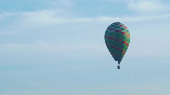 Colorful hot air balloon floating up in blue sky, birds flying trough the frame, medium distant shot alt