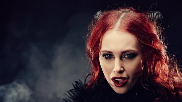 Woman Smiling Devilishly and Cast a Spell. Portrait Witch Witch with Red Hair and Devil Horns alt