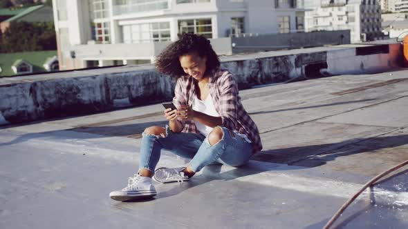 Fashionable young woman on urban rooftop using smartphone alt