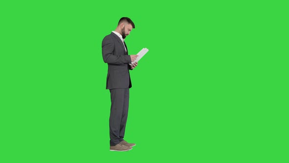 Businessman Standing and Reading Docs Seriously on a Green Screen, Chroma Key. alt