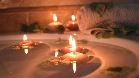 relaxing spa background with candles floating in the bath water, some green petals and a towel near alt