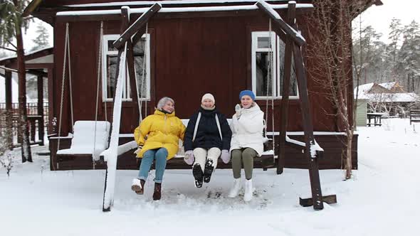 Three Adult Women Ride on a Swing with Snow Around Them