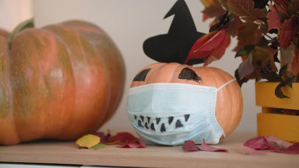 Halloween Decoration Pumpkin with Hat and Protective Medical Mask on Face Stands on Table with alt