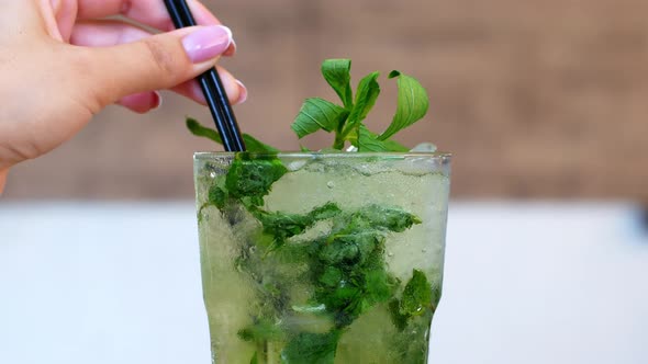 Refreshing summer mojito cocktail in a glass. Woman hand takes a glass of tropical drink mojito