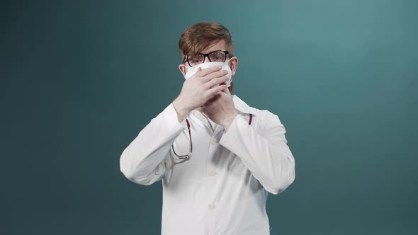 Man with Beard with Serious Face in Laboratory Coat Puts Protective Mask on Green Lab Background