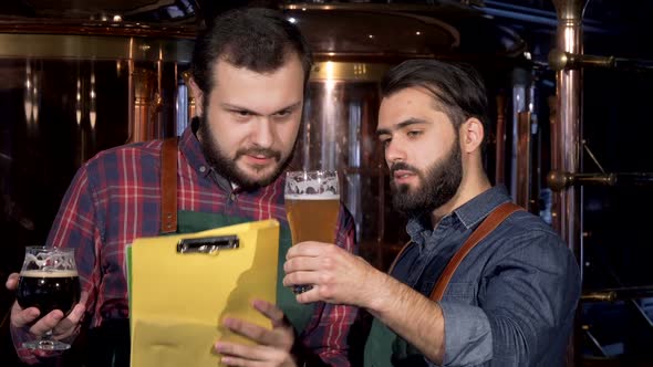 Two Male Brewers Examining Delicious Craft Beer They Manufacture Together alt