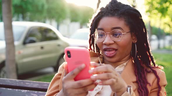 Young African American Woman Sitting on a Bench in the City and Using Her Smartphone