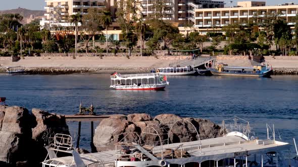 Traditional boat crusing through the Nile river with building in the bacground and rocks in the fore alt
