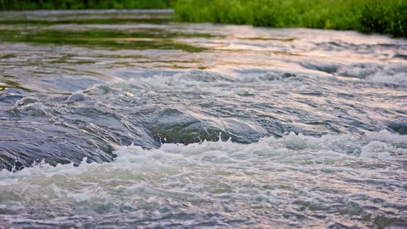 the Flowing Water of a Summer River with a Small Rapid Waterfall in Slow Motion at Daylight alt