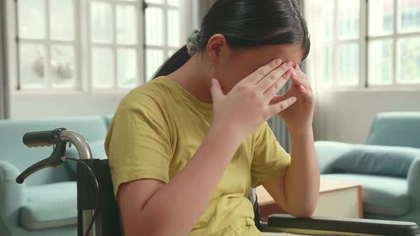 Close Up Of Disappointed Asian Kid Girl Sitting In A Wheelchair In Living Room At The House alt