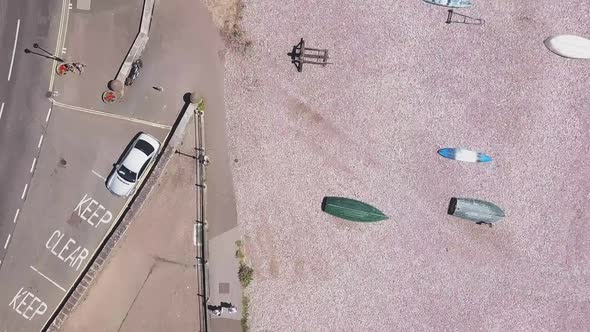 Aerial Top Shot STATIC CROP, flying over a pebble beach full of boats and a street with parked cars alt