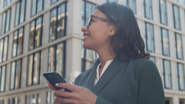 Cheerful Businesswoman Using Cellphone Outside alt