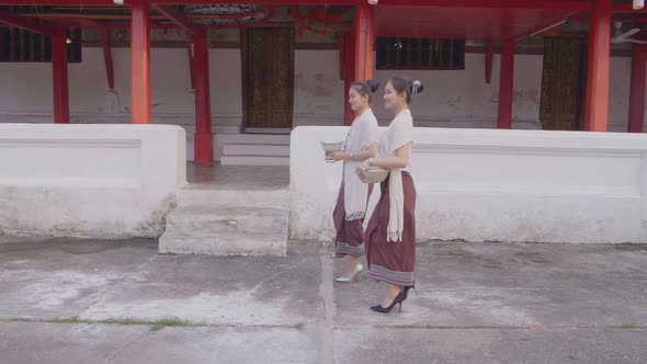 Girls In Thai Traditional Dress Walking Near Temple With The Water Bowl alt