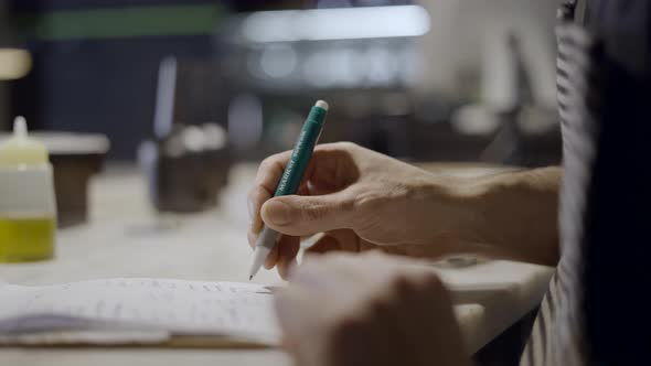 Side Closeup of Male Hand Writing on Notepad at Restaurant Counter alt