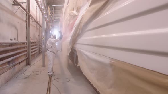 A Man in a Protective Suit and a Respirator Covers the Car with a Protective Layer of Varnish Using alt
