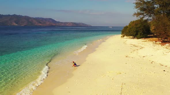 Single guy fishing alone on beautiful resort beach break by blue green sea with white sand backgroun alt