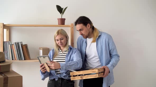 Moving Day Happy Couple in New House Unpacking Looking at Photo Frame with Photo and Nostalgia alt