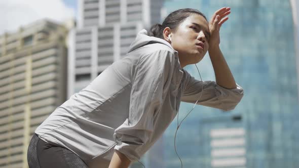 Asian fitness runner sportswomen tired after running and having building background.