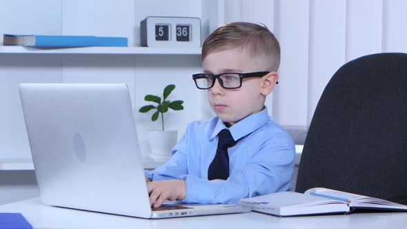 Boy in Glasses Is Typing on a Laptop and the Data Recorded in Notes alt
