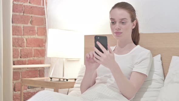 Attractive Redhead Young Woman Using Smartphone in Bed alt