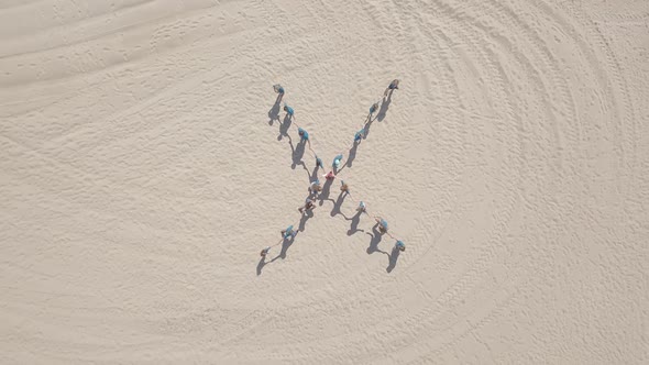 Aerial view of children stand in shape of cross then hug.Teenager sport team play on sand beach, sea