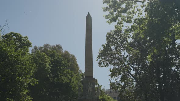 Tall landmark obelisk in downtown Madrid surrounded by green trees, motion view alt