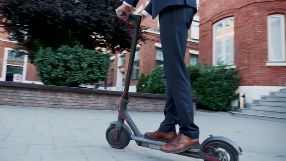 Unrecognisable Man in Business Suit Coming to Work on Electric Scooter alt