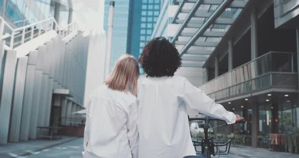 Woman leans on another woman's shoulder and together they look at the view of buildings alt