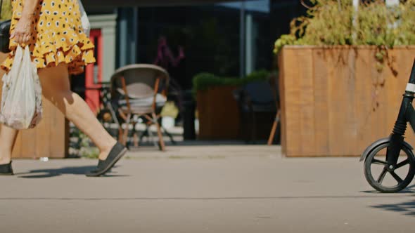 Closeup Legs Walk Down the Street Past the Camera the Girl Rides a Scooter alt