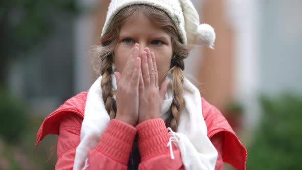 Portrait of Charming Teenage Caucasian Girl Blowing on Palms Rubbing Hands Standing Outdoors on alt