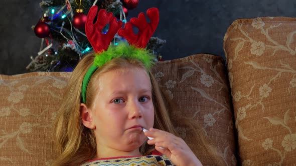 Sad sick child with thermometer in mouth in New Years eve Cute little girl in festive red deer horns