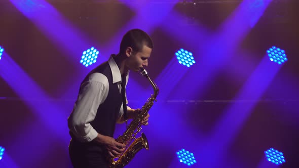 A Young Retro Stylish Guy Plays on the Golden Shiny Saxophone in the Blue Spotlights on Stage alt