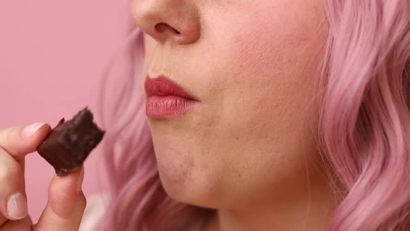 Portrait of Young Woman Biting in a Pieace of Chocolate Waffle Candy Isolated Over Pink Background