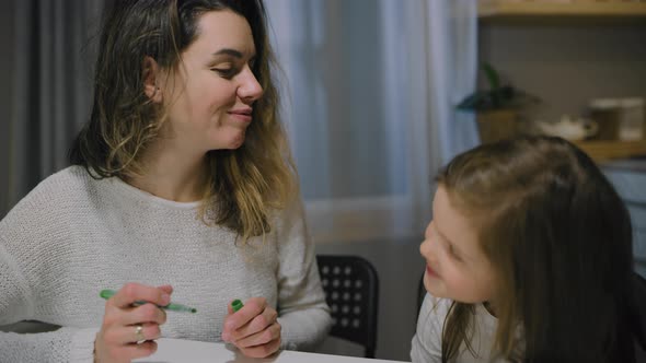 A Mother and a Small Daughter Draw Drawings on Paper in the Kitchen with Markers